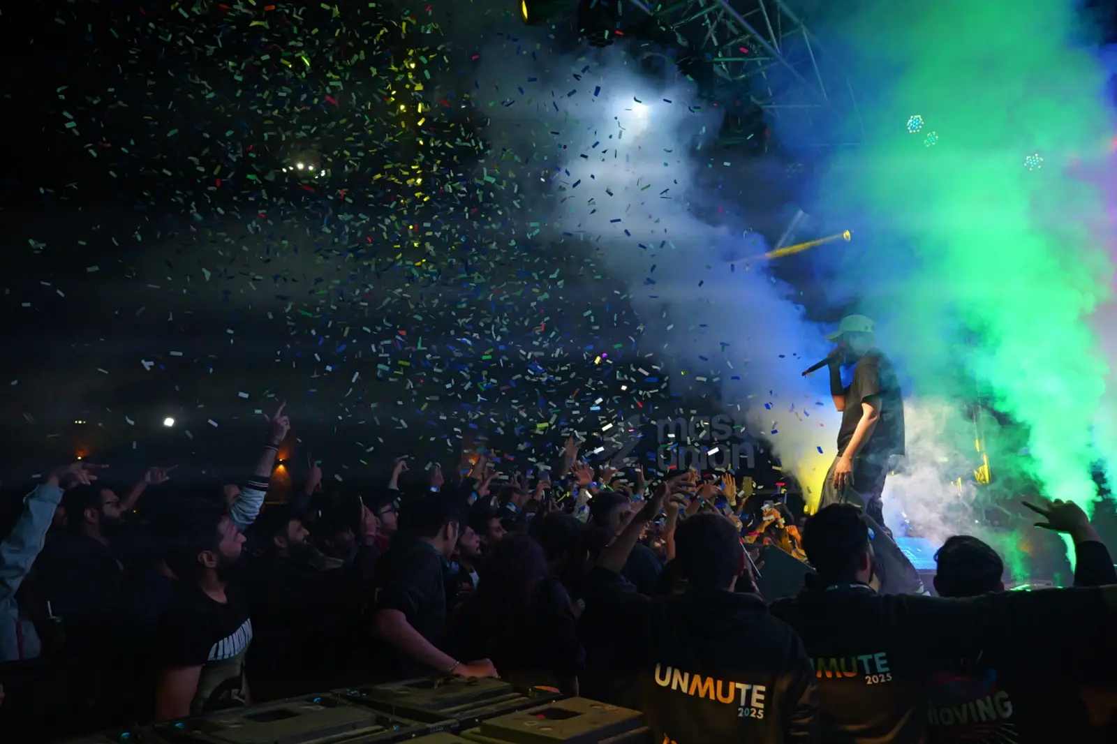 A crowd under stage lights and green smoke at night