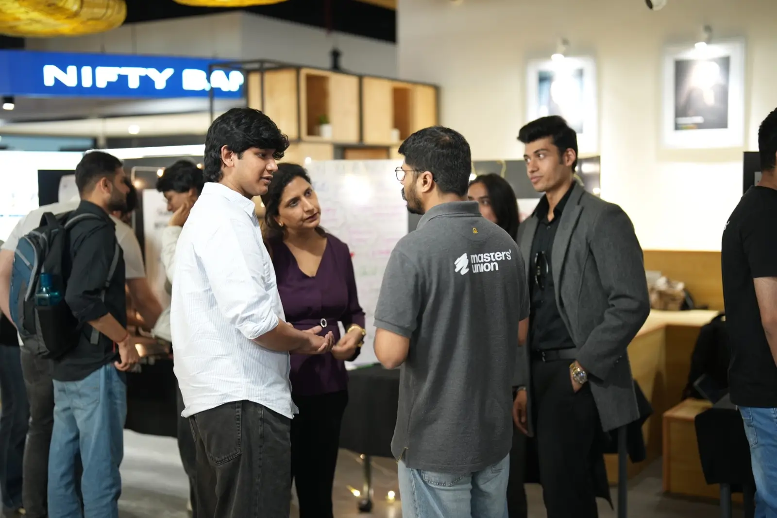 Students in conversation beneath a Nifty market ticker